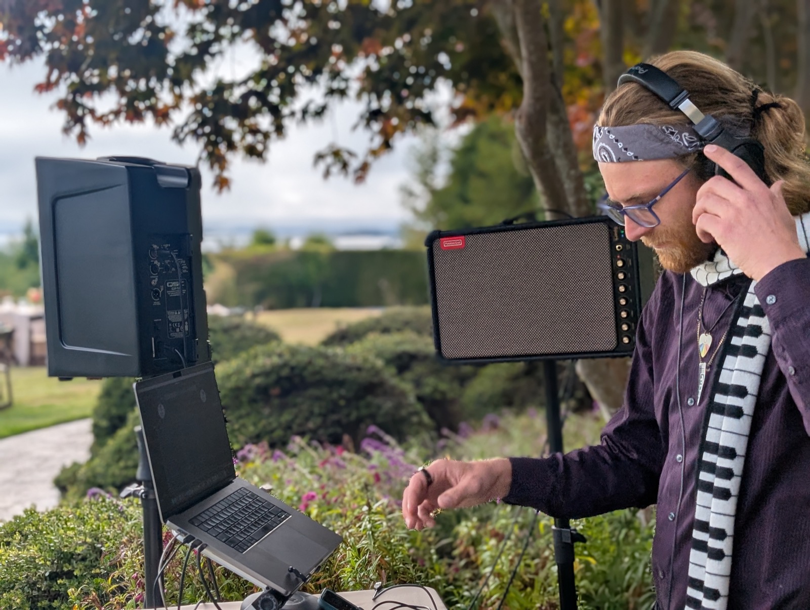 Kieran Specht DJing outdoors, wearing his signature piano-key scarf and headphones