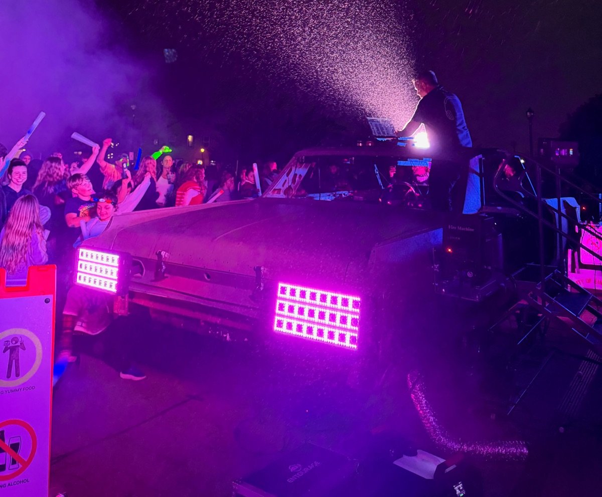 Kieran Specht running a DJ set from atop a light-rigged car in the rain, purple stage lighting over the crowd